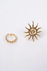 Set de dos anillos de metal dorado. Uno de ellos presenta un diseño de sol con textura irregular y el otro tiene un diseño de eslabones en forma de conchas marinas.