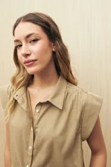 Camisa color beige con cuello clásico, abotonada al frente y sin mangas. Presenta detalle de bordado en los hombros.