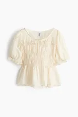 Blusa color beige, de mezcla de lyocell, con escote redondo, mangas cortas abullonadas y busto fruncido con tiras decorativas.