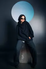 Buzo negro de corte oversize con cuello alto tipo polera y capucha integrada. Presenta mangas largas con puños ajustados y un diseño holgado en el cuerpo.