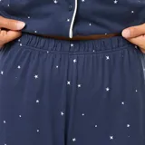 Pijama largo de dos piezas azul marino con estampado de estrellas blancas y ribetes blancos. Incluye camisa de manga larga con cuello y botones, y pantalón largo de corte recto.
