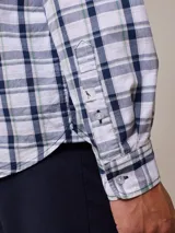 Camisa de manga larga para hombre, confeccionada en algodón con efecto peach (textura suave). Presenta un estampado de cuadros vichy en tonos azul marino y blanco, cuello con botones y un bolsillo de parche en el pecho izquierdo.