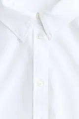 Camisa blanca de corte relajado, cuello clásico, mangas largas y cierre frontal con botones.