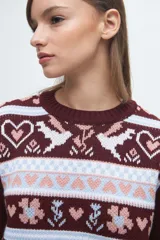 Buzo tejido de punto con diseño jacquard que presenta motivos de corazones, flores y aves en tonos bordó, blanco y celeste. Posee cuello redondo, puños y ruedo acanalados.