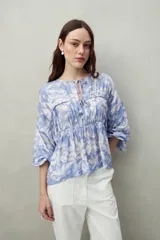 Blusa estampada de caída fluida con cuello redondo y lazos frontales, diseño con cortes horizontales y frunces, mangas largas con puños elastizados.