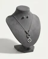 Set de joyería en acero compuesto por un collar con dije circular de trébol de cuatro hojas y un par de aros tipo bolita. El collar presenta una cadena con esferas decorativas en la parte central.