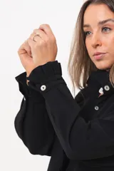 Camisa de manga larga color negro, con cuello camisero, cierre frontal con botones y detalle de volados en la cartera y los puños.