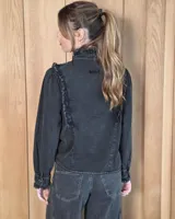 Camisa de denim celeste con cuello alto con volados, botonadura frontal y detalles de volados verticales a lo largo del frente. Cuenta con mangas largas abullonadas y puños con volados.