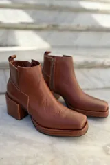 Bota corta de cuero color suela, con taco cuadrado y punta cuadrada. Presenta una plataforma con textura grabada y cierre lateral.
