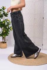 Pantalón wide leg de denim negro desgastado, de tiro medio con doble botón y corte amplio en las piernas con costuras frontales.