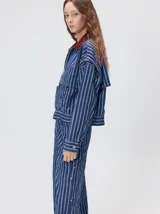 Campera de denim a rayas verticales con cuello de pana en color bordó. Presenta cierre frontal, mangas desmontables con cierre en los hombros, canesú en el pecho y bolsillos de parche cuadrados.