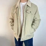 Chaqueta de pana color beige con interior y cuello de corderito sintético. Presenta cierre frontal con botones, dos bolsillos superiores con solapa y bolsillos laterales.