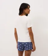 Pijama corto de dos piezas de la marca Lov, confeccionado en viscolycra. Incluye una remera blanca de manga corta, cuello redondo y un bolsillo frontal a cuadros, combinada con un short azul marino con estampado a cuadros y diseño de osos, con cintura elástica.