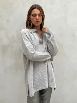 Sweater de punto acanalado color gris, con cuello polo y escote en V. Diseño holgado con mangas largas y aberturas laterales en el dobladillo.