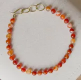 Collar corto con cuentas de piedra cornalina ágata y dije colgante de bronce con forma de sol.