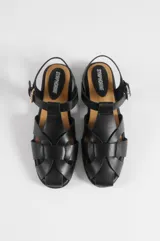 Sandalias planas negras estilo romano de cuero vegano, con diseño de tiras cruzadas, talón cerrado y hebilla metálica dorada ajustable en el tobillo.