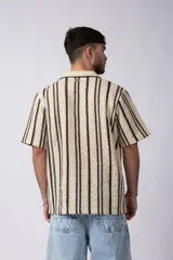 Camisa de manga corta tejida al crochet con diseño de rayas verticales negras sobre una base color crudo. Presenta cuello solapa y cierre frontal con botones.
