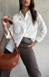 Camisa blanca de manga larga con cuello clásico y cierre frontal de botones. Presenta un diseño con paneles de encaje bordado en la parte superior delantera, confeccionada en tejido con textura.