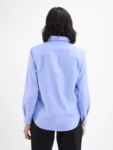 Camisa de corte clásico en tejido oxford color azul, con cuello camisero, cierre frontal de botones, manga larga con puños abotonados y un bolsillo frontal en el pecho.