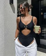 Malla enteriza negra con escote en V, tirantes finos, abertura cut-out en el abdomen y detalle de argolla dorada en el centro del busto. La parte inferior presenta fruncido en los laterales.