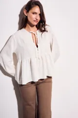Blusa color crudo de viscosa y lino con bordados en el frente, escote con lazo y mangas largas. Corte holgado con frunce en la cintura.
