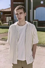 Camisa de manga corta a rayas verticales color crudo y verde, con cuello resort, corte holgado y cierre frontal con botones.