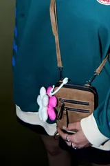 Llavero colgante con forma de flor acolchada, compuesto por múltiples pétalos blancos y dos flores rellenas de color rosa fucsia. Se sujeta mediante un cordón trenzado blanco con un gancho de plástico blanco.