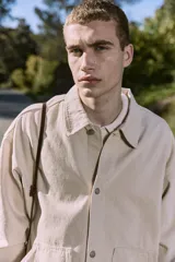 Camisa de denim color beige claro, corte amplio, cuello clásico, cierre frontal con botones y mangas largas. Confeccionada en tejido denim de sarga con acabado acid wash.