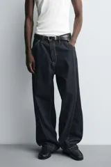 Jeans de denim oscuro, corte ancho (baggy fit) y tiro medio, con costura central girada en el frente de ambas piernas. Presenta pespuntes en color caramelo.