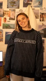 Buzo de tejido de punto con diseño a rayas verticales en color azul marino y blanco. Presenta cuello redondo, puños y ruedo acanalados, y un recuadro central con la inscripción 'GLASSY WAVES' tejida en el frente.