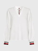 Blusa de manga larga Tommy Hilfiger confeccionada en algodón orgánico. Presenta un cuello en V amplio y puños elásticos con el diseño de rayas distintivo de la marca en colores blanco, rojo y azul marino.