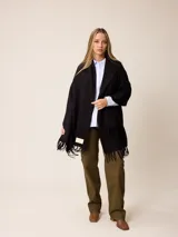 Pashmina de textura suave y color crema, con diseño liso y terminaciones en flecos en los extremos. Incluye una etiqueta decorativa en una de las esquinas.