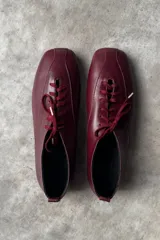 Zapatos tipo flat de cuero color bordó, con diseño de punta cuadrada y cordones al tono.