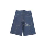 Bermuda de jean rígido color azul oscuro, corte baggy, con costuras contrastantes en color camel. Presenta un bordado estilizado en hilo blanco en el bolsillo trasero derecho.