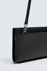 Cartera tipo bandolera de color negro con acabado texturizado. Cuenta con un compartimento principal con cierre de cremallera, interior con dos compartimentos adicionales y asa de hombro ajustable y extraíble.