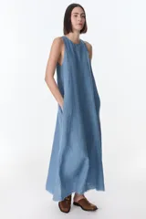 Vestido largo sin mangas, color azul claro, de corte amplio y holgado, con cuello redondo y bolsillos laterales. El ruedo presenta un acabado deshilachado.