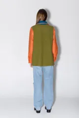 Camisa de paño confeccionada en lana, con diseño multicolor que combina paneles en verde oliva, naranja y azul. Presenta cuello clásico, cierre frontal con botones, bolsillos aplicados y detalles de bordados artesanales a mano en los bordes.