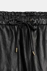 Pantalón de tiro alto confeccionado en material efecto piel, con cintura elástica ajustable mediante cordones, bolsillos delanteros y bolsillos de plastrón en la parte trasera.