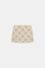 Minifalda de tiro medio confeccionada en ante color beige, decorada con aplicaciones de tejido tipo crochet blanco formando un patrón de rombos. Cuenta con cierre de cremallera oculta en la costura.