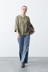 Camisa de color celeste claro con silueta relajada y mangas largas. Presenta un cuello redondo con pequeña abertura frontal y botones, además de un delicado trabajo de tablas en los hombros que aporta textura al diseño.