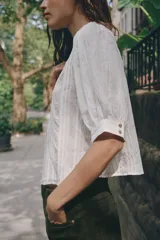 Blusa blanca de cuello alto con detalles de puntilla, manga corta abullonada y cierre posterior con botón.
