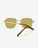 Lentes de sol con marco metálico dorado de forma geométrica y cristales en tono amarillento. Presentan patillas finas con terminales en color marrón.