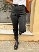 Jean mom fit de tiro alto color negro con costuras en contraste. Presenta diseño de cinco bolsillos, cierre frontal con botón metálico y costuras verticales decorativas en el frente que estilizan la figura.