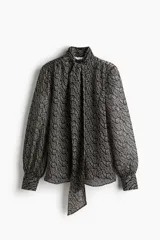 Blusa de gasa transparente con estampado paisley en tonos verde, beige y negro. Presenta cuello alto con moña, abertura en V frontal, frunces en los hombros, mangas globo largas y puños abotonados.