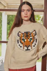 Sweater de lana color crudo con diseño de cabeza de tigre bordado en el frente. Presenta cuello redondo, mangas largas con hombros caídos y puños acanalados.
