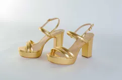 Sandalia de cuero con plataforma y taco cuadrado alto. Presenta una tira delgada en el tobillo con cierre de hebilla metálica y dos tiras acolchadas en la parte frontal.