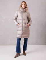 Campera puffer larga de acabado satinado en tono beige. Presenta un diseño capitoneado horizontal, cierre frontal bidireccional y un amplio cuello envolvente revestido en piel sintética. Incluye bolsillos laterales funcionales con cierre y logo metálico en la manga.