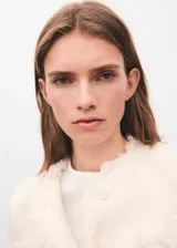 Chaqueta de tweed color crema con cuello redondo, cierre frontal con botones y dos bolsillos de parche delanteros. Presenta terminaciones deshilachadas y forro interior.