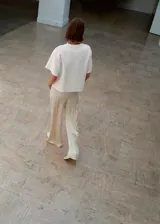 Pantalón de corte recto y tiro medio, confeccionado en tejido satinado con forro interior. Presenta cintura elástica, dos bolsillos laterales y aberturas en los bajos.