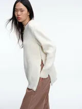 Sweater de tejido de punto acanalado en color blanco, con cuello redondo, mangas largas y corte holgado. Presenta un diseño minimalista y contemporáneo.